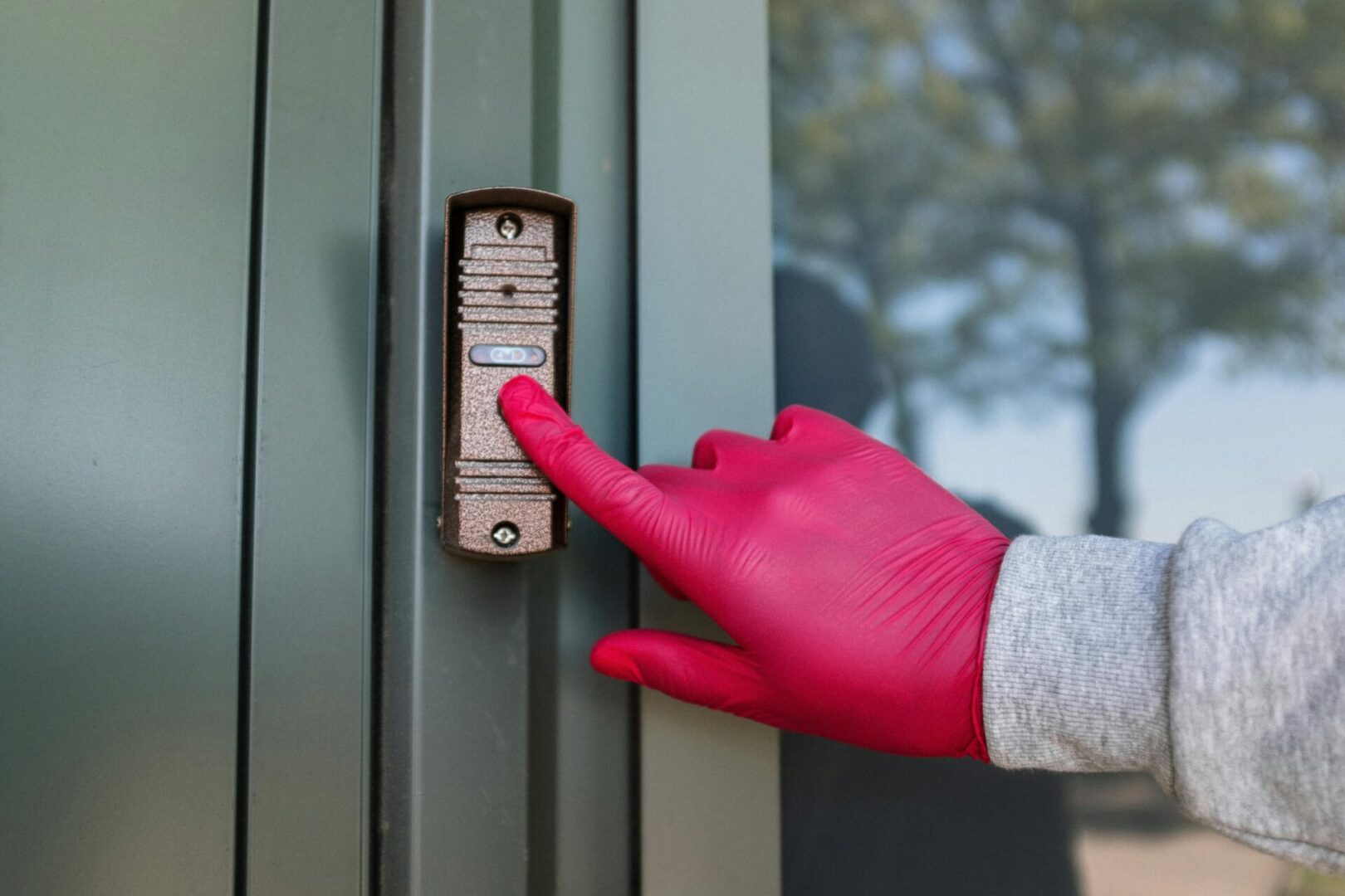 A person wearing gloves and using a door bell